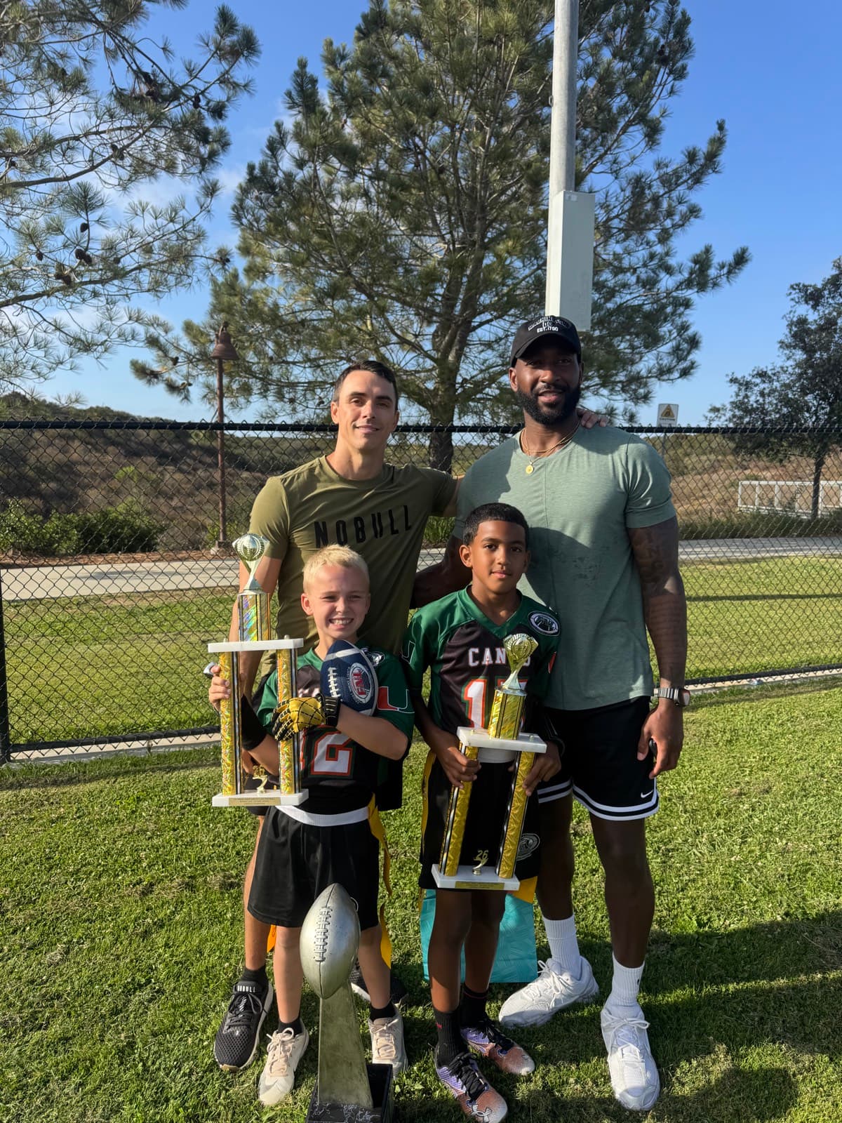 Coach P (Paul Clotar) and Coach Q (Nate Queen) with their sons on the field after a youth football championship win.